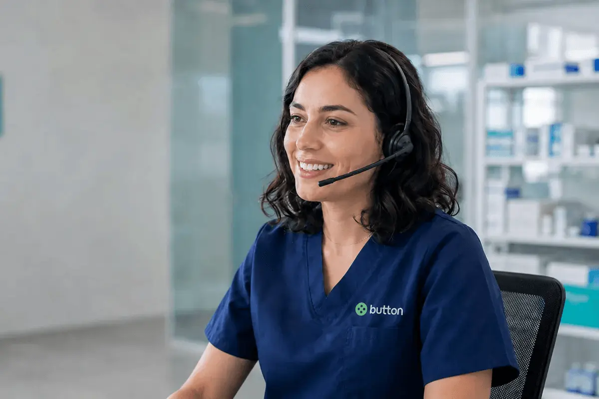 Button customer support specialist wearing a headset and smiling while helping a healthcare customer in a bright office